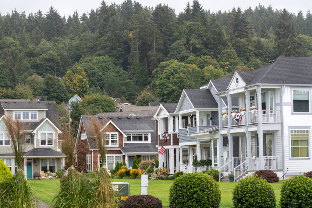 A craftsman-style home in Oregon with a well-maintained lawn and tree-lined background, viewed during a sunny afternoon.